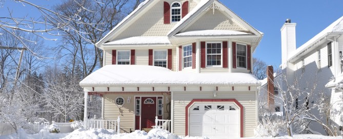 White house with maroon shutters and a maroon front door. There are blue skies and plenty of snow on the ground.