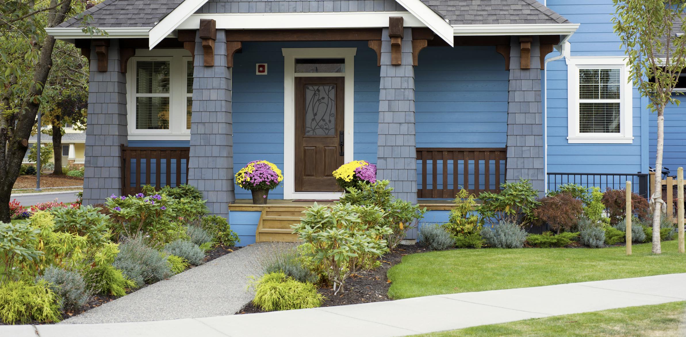 Blue house with wood porch and flowers in buckets framing the door.