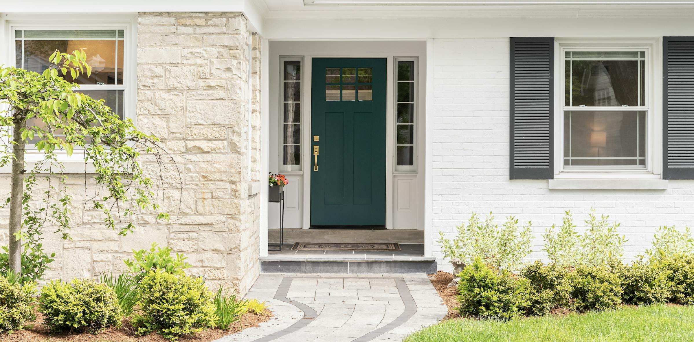 White house with stone, black shutters, and a dark blue front door.