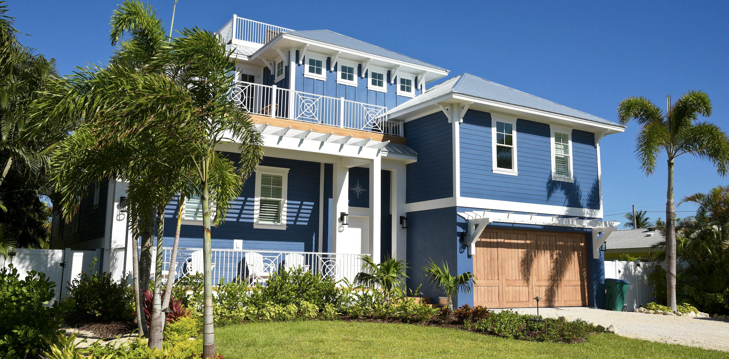 Blue house with green grass and palm trees in the yard.