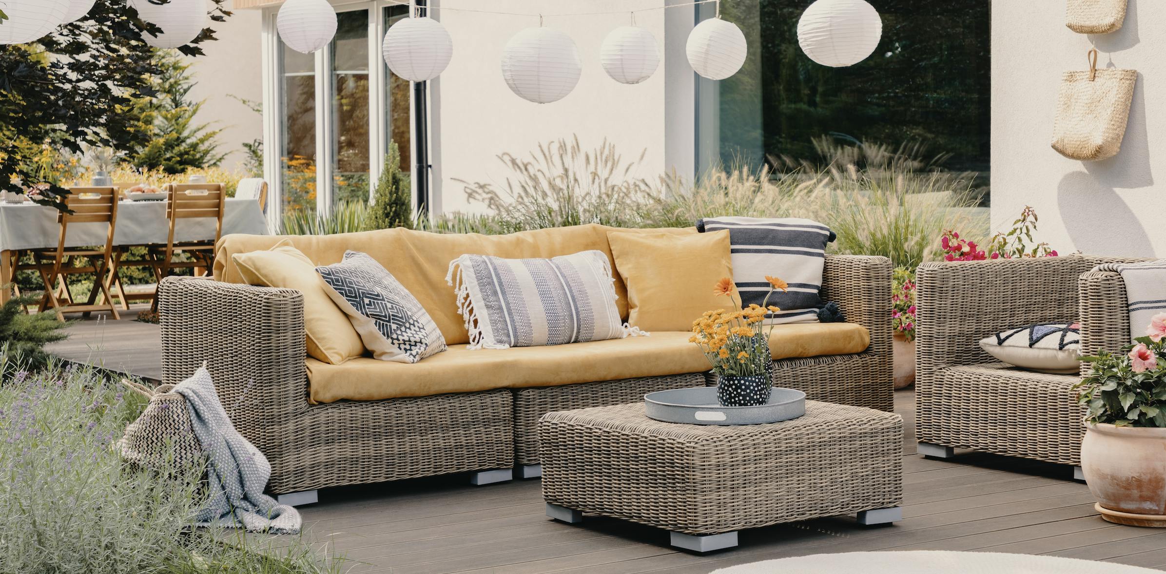 Summertime patio with a yellow sofa, plants, and white lights hanging overhead.