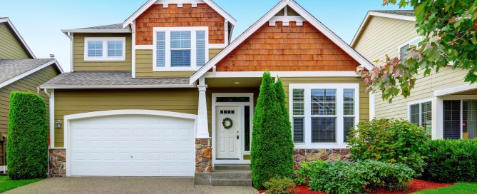 Green and brown house with green trees lining the driveway.