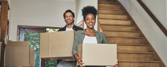 Two people moving into a new house and carrying boxes.