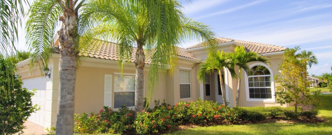 Home in Florida with palm trees and orange flowers in the green grassy yard.