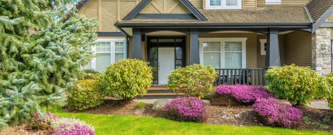 Home in springtime with green trees, green grass and pink flowers in the yard.
